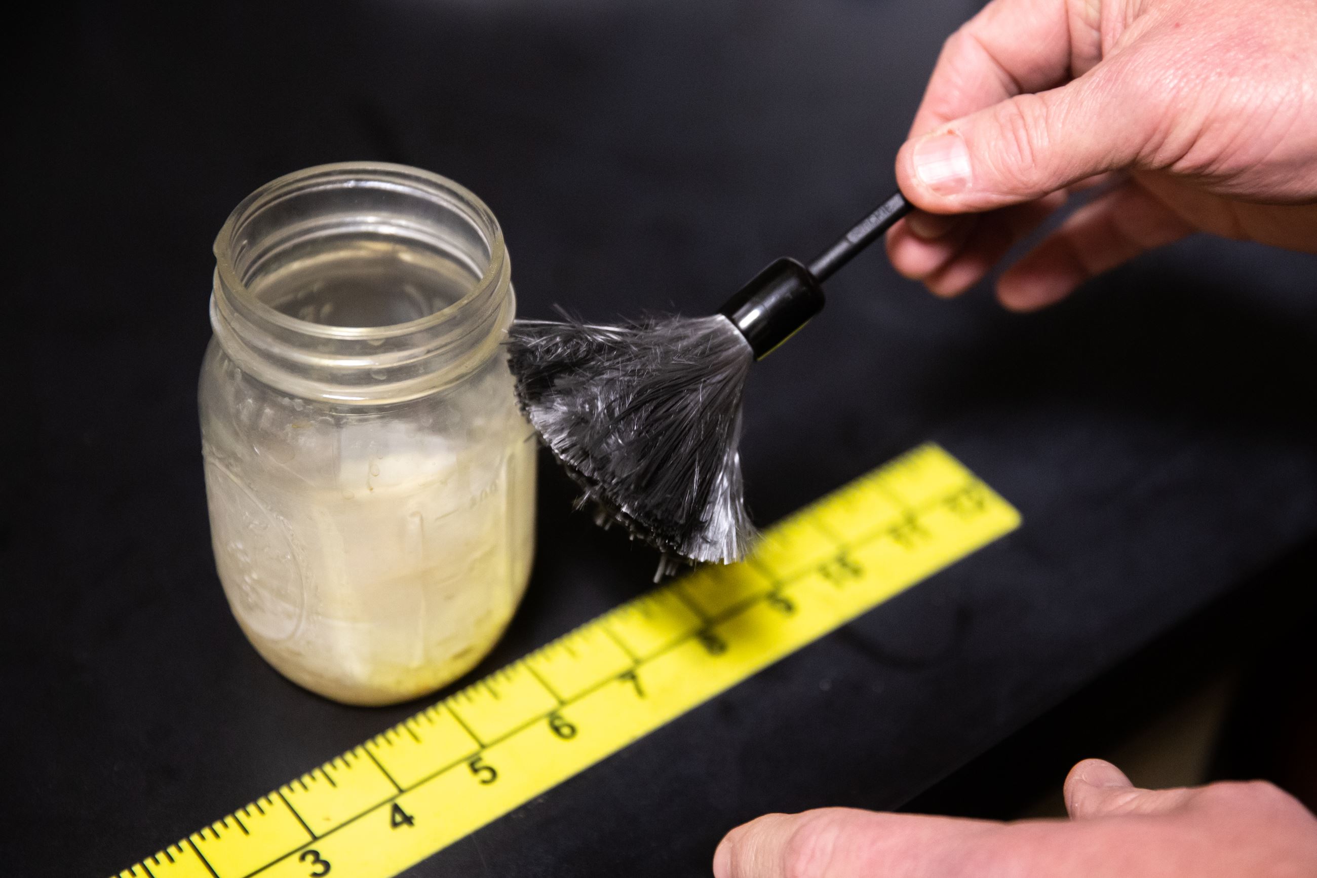 Hand holding brush, above ruler next to glass jar